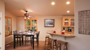 Un espace repas comprenant une table et des chaises en bois, un lustre, ainsi qu’un coin cuisine avec des armoires et un plan de travail en bois.