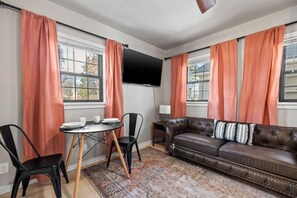 Une pièce comprenant un canapé en cuir, une table ronde avec des chaises et un téléviseur à écran plat fixé au mur.