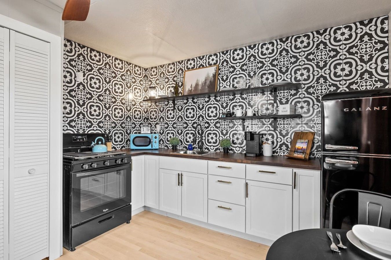 Een keuken met een decoratieve spatwand, een zwart fornuis, witte kasten en een zwarte koelkast.