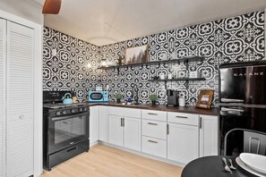 A kitchen with a patterned backsplash, a black stove, white cabinets, and a black refrigerator. - Cottage #7- Spearfish Orchard Creek Cottages (Spearfish)