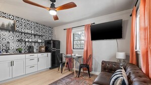 Un espacio habitable compacto con kitchenette, zona de comedor, sofá y televisor de pantalla plana montado en la pared.