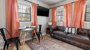 Una sala de estar con un sofá de cuero, dos sillones, una mesita redonda y un televisor de pantalla plana montado en la pared.