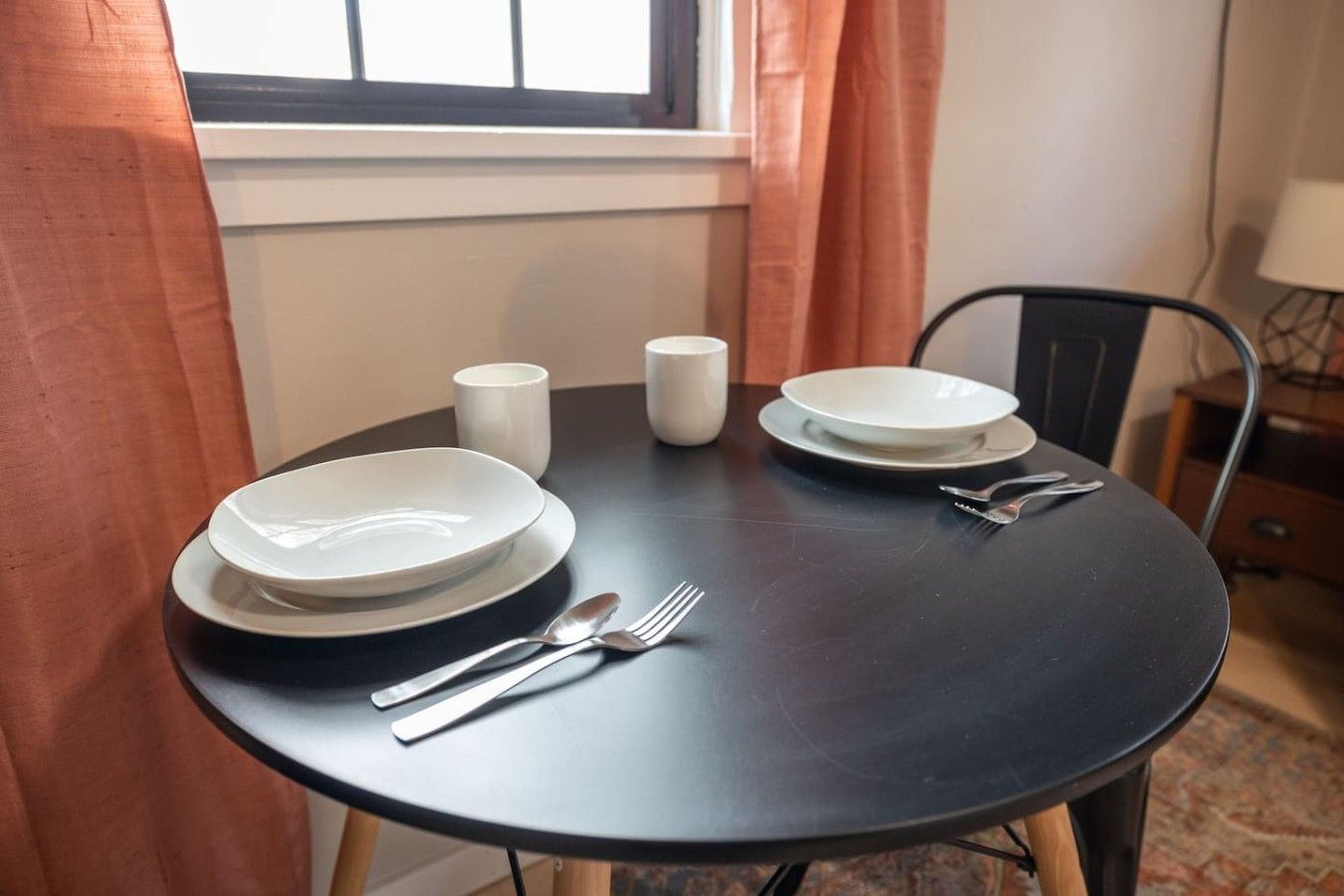 A round dining table with white plates, cutlery, and two white cups.