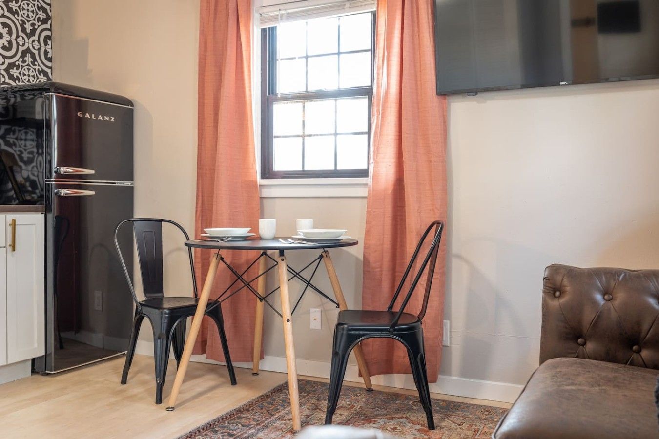 A compact living space with a kitchenette, a dining table with chairs, a sofa, and a window with curtains.