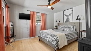 Un dormitorio con cama, ventilador de techo, televisor, chimenea y ventana con cortinas.