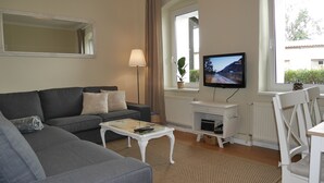 Een woonkamer met een grijze bank, een witte salontafel, een televisie en een raam met gordijnen.