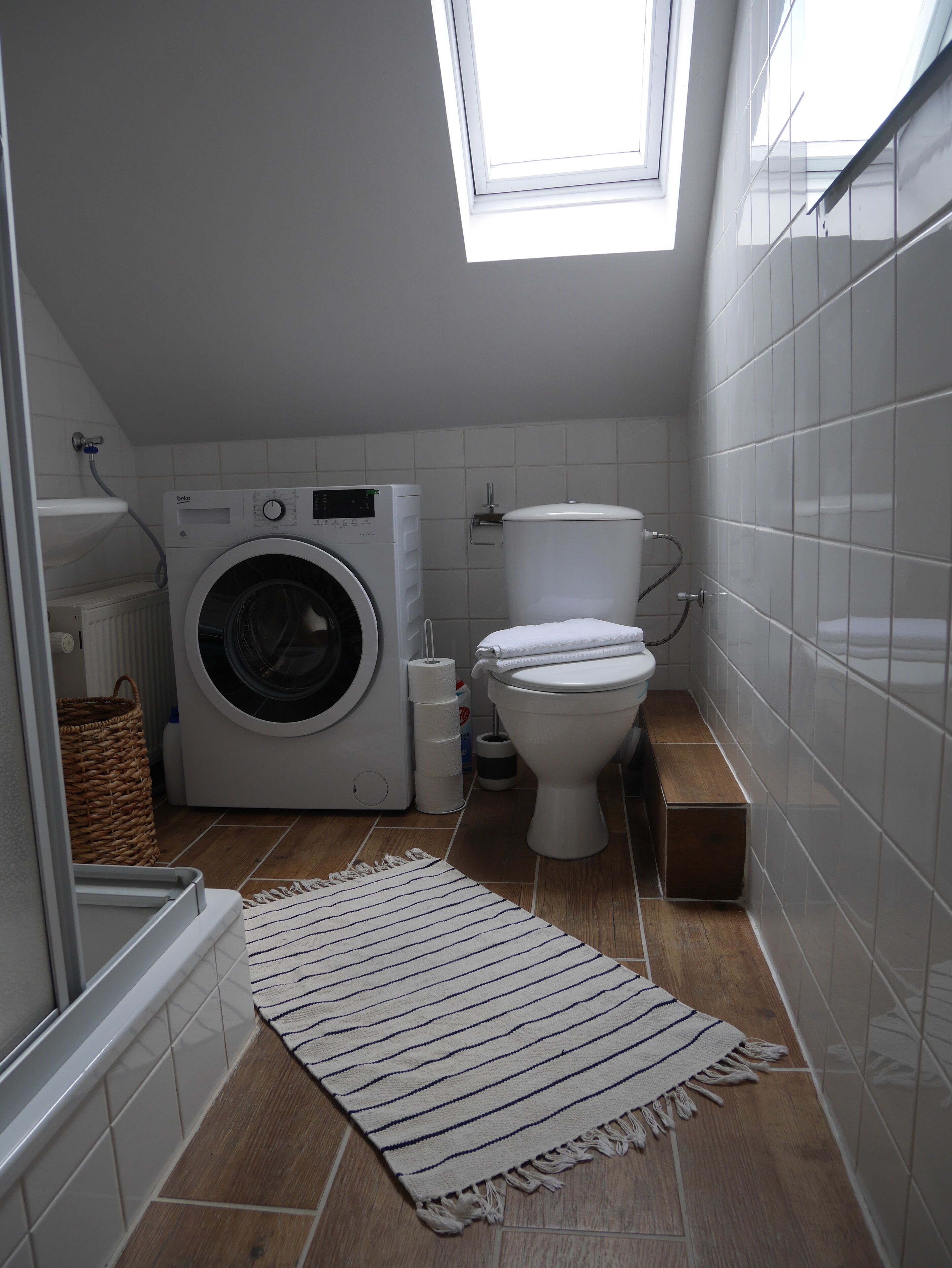 Een kleine wasruimte met een wasmachine, toilet en een klein houten bankje.