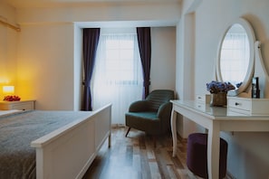 A bedroom with a bed, a desk, a chair, a mirror, and a window with curtains.