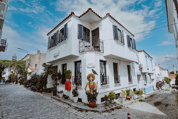 A white building with a balcony, potted plants, and a street view.