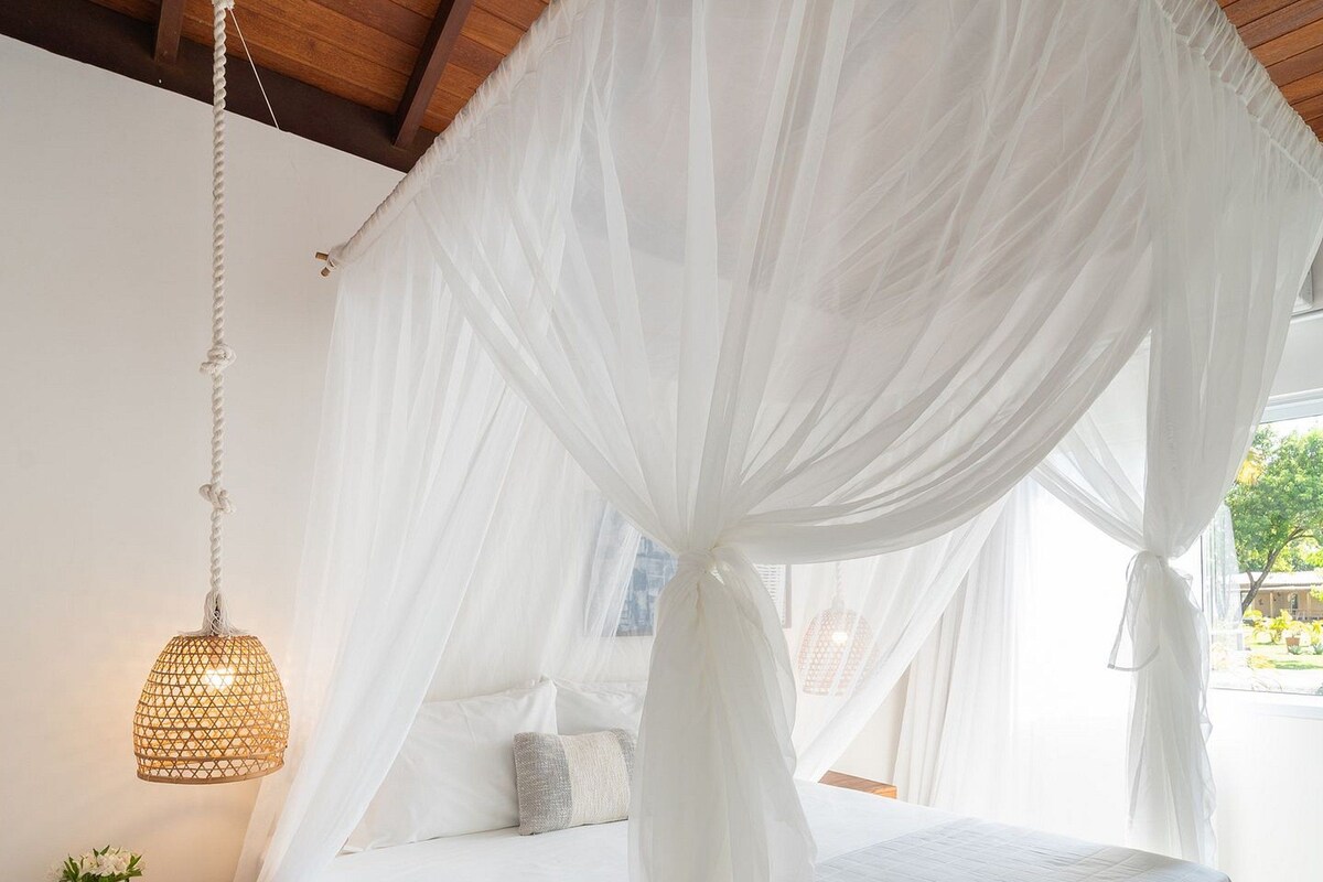 Un dormitorio con cama a dosel, lámpara colgante y mesita de noche con una planta.