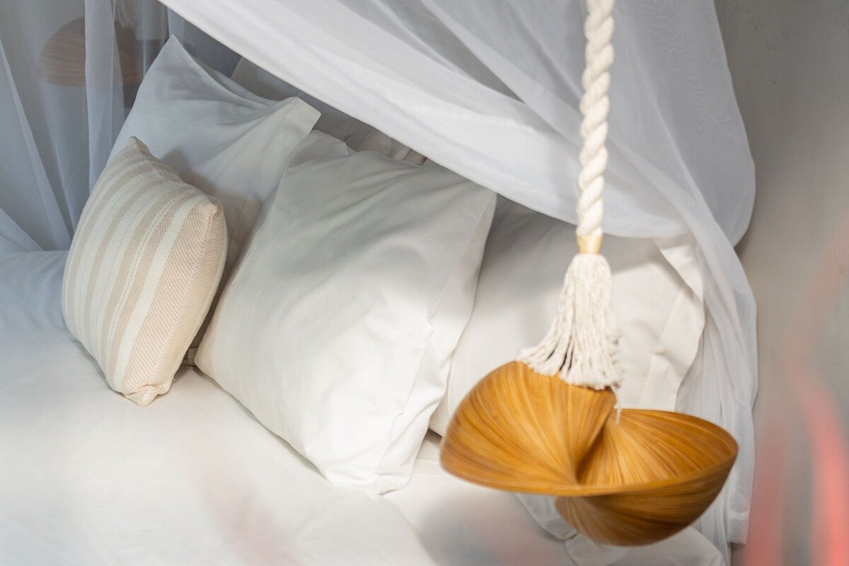 Cama com roupa de cama branca e uma cadeira suspensa.