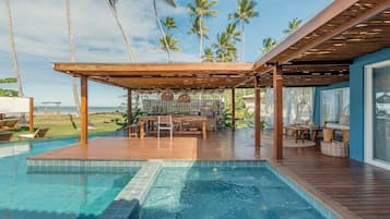 A wooden deck with a pool, outdoor furniture, and a view of the ocean and palm trees.