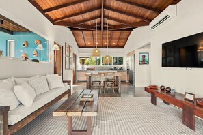 A spacious living area with a wooden ceiling, a sofa, a dining table, and a kitchen in the background. - Orixás Residence (Cairu)