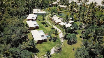 An aerial view of a resort with multiple bungalow-style buildings, a swimming pool, and a beach in the background.