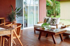 A wooden deck with a sofa and chairs, a table with a plant, and a view of greenery through a glass door. - Orixás Residence (Cairu)