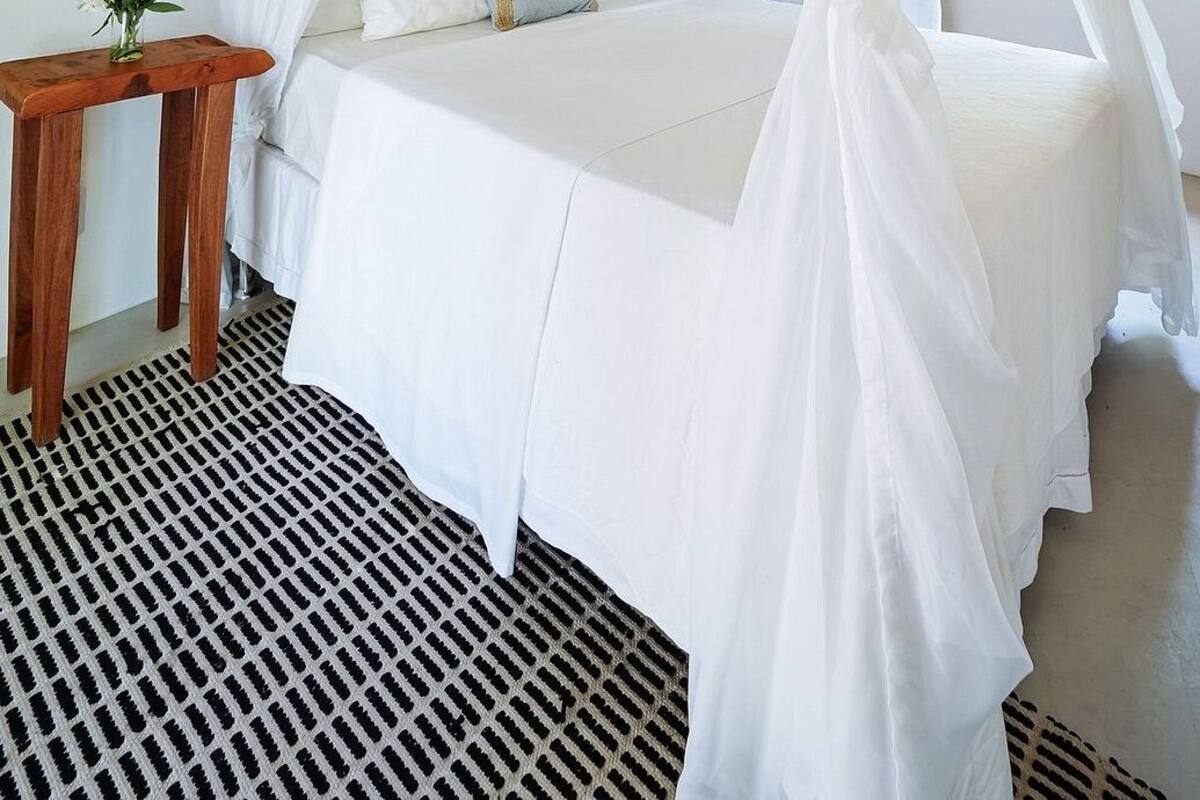 A bed with a white canopy, a wooden nightstand with a vase of flowers, and a patterned floor.