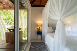 Un dormitorio con cama a dosel, una mesita de noche con lámpara y vistas al exterior.
