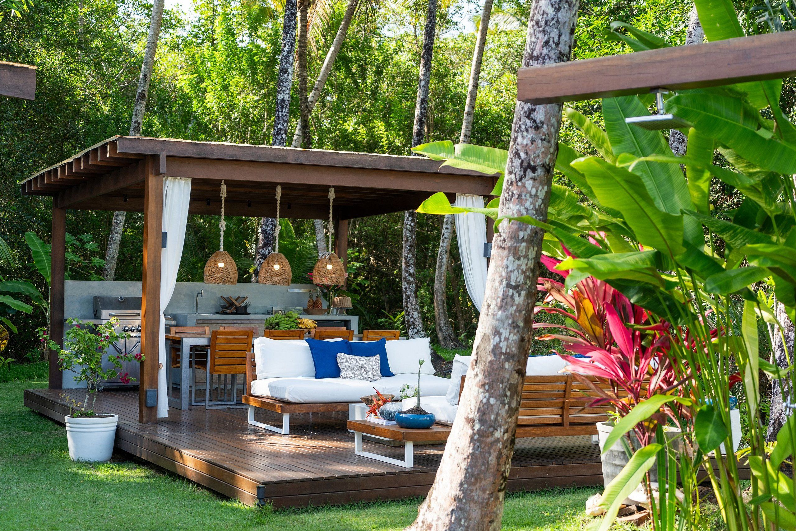 An outdoor patio with a wooden deck, a white sofa, a dining table, and a hanging light fixture.