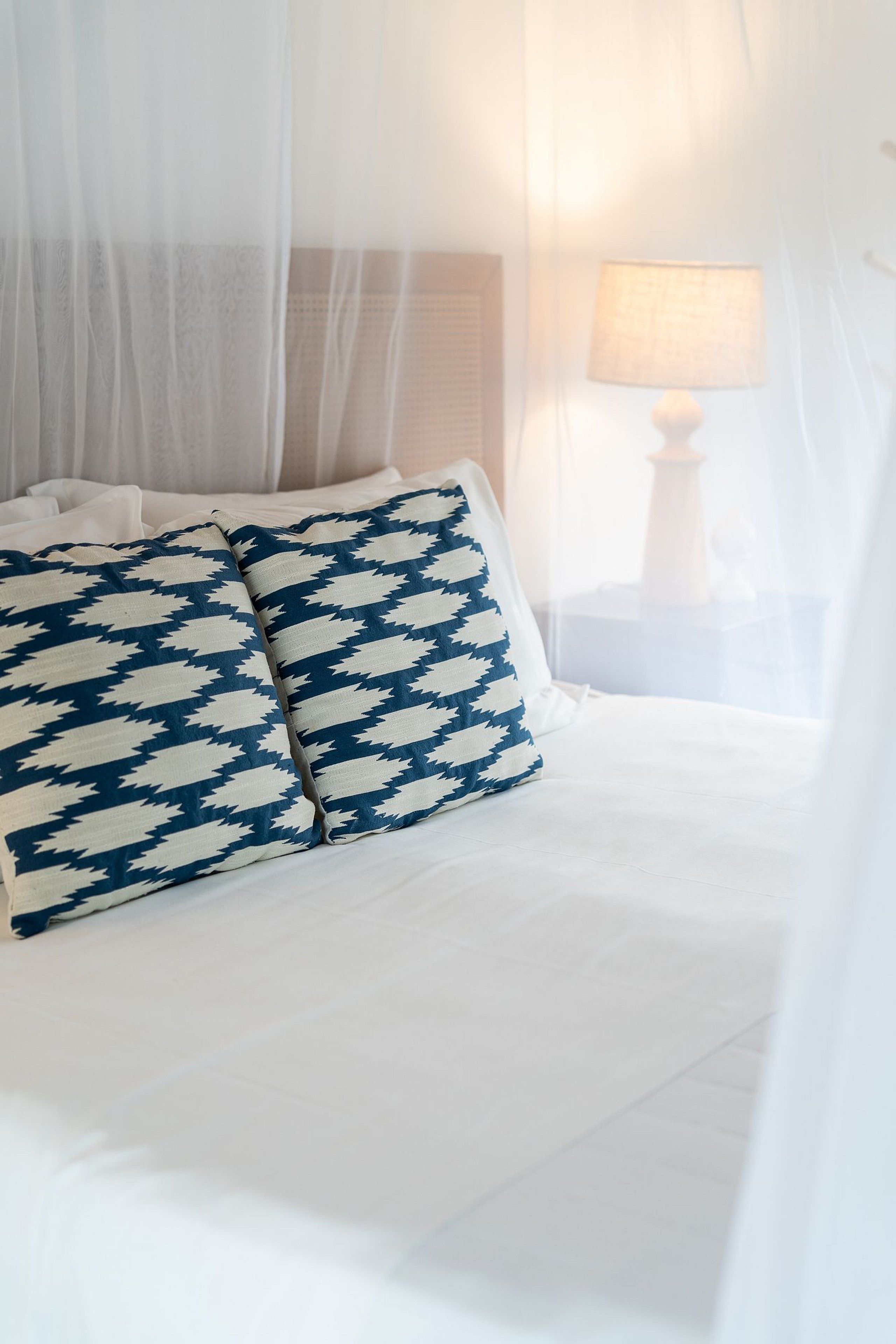 A bed with white bedding and a blue and white patterned pillow.