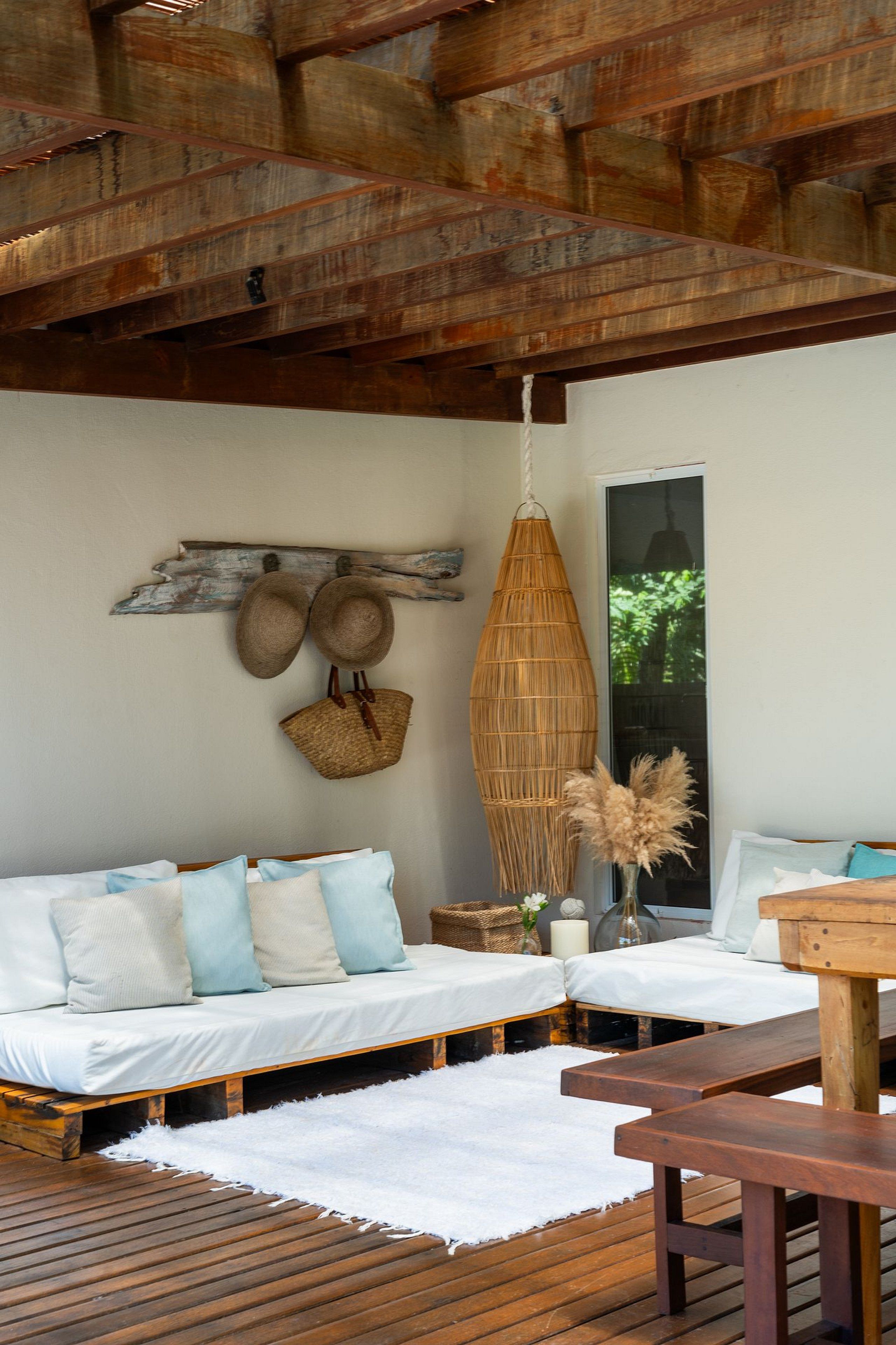A cozy room with a wooden ceiling, a bed with white and blue bedding, a hanging basket, and a wooden bench.