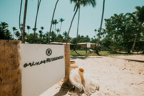 A resort with a sandy beach, palm trees, and a sign for 'Orxas Residences'. - Orixás Residence (Cairu)