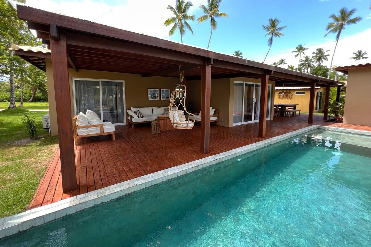 Uma área de piscina com deck de madeira, uma cadeira suspensa e um sofá.