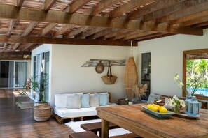 A spacious living area with a wooden ceiling, a sofa with cushions, a dining table with a fruit bowl, and a hanging basket. - Orixás Residence (Cairu)