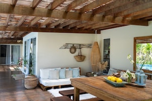 Un espacio habitable amplio con techo de madera, un sofá con cojines, una mesa de comedor con frutero y una cesta colgante.