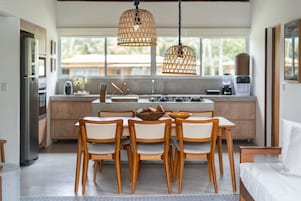 Una cocina moderna con comedor, que cuenta con una isla central, sillas de madera e iluminación colgante de mimbre.
