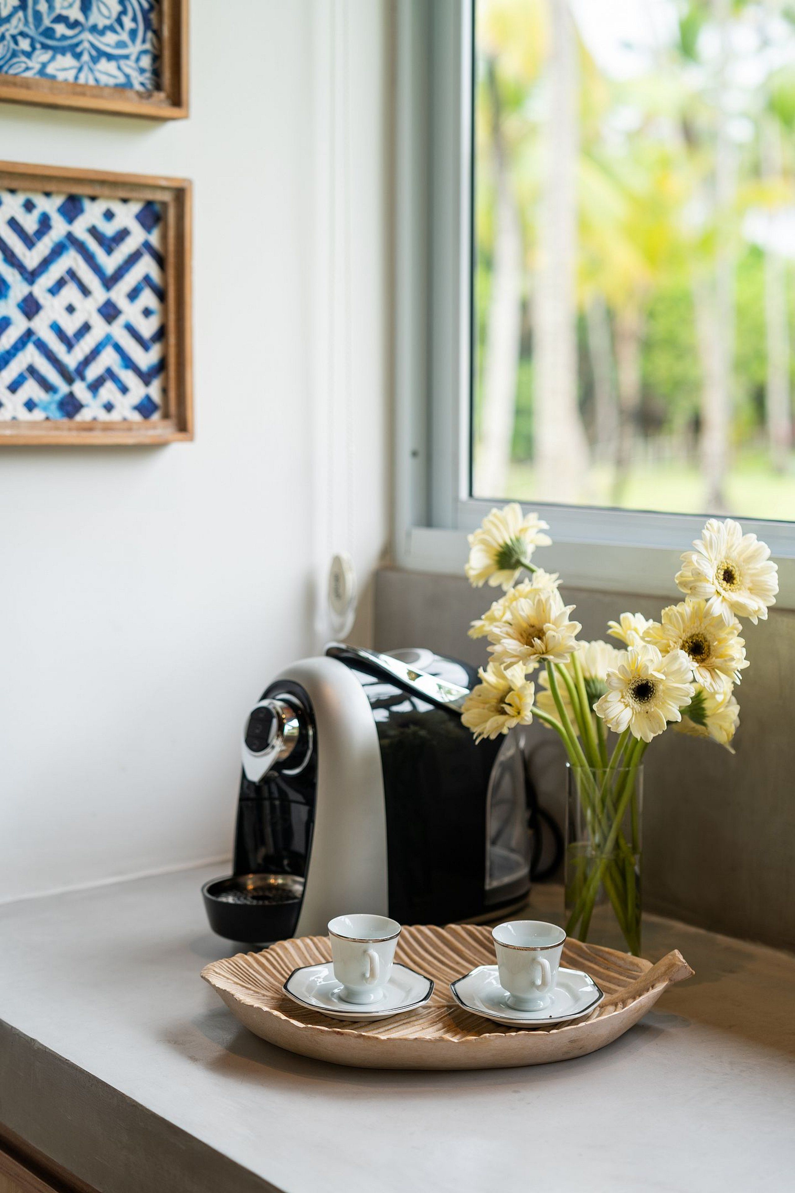 A tray with two cups and saucers, a vase with flowers, and a bag on a windowsill.