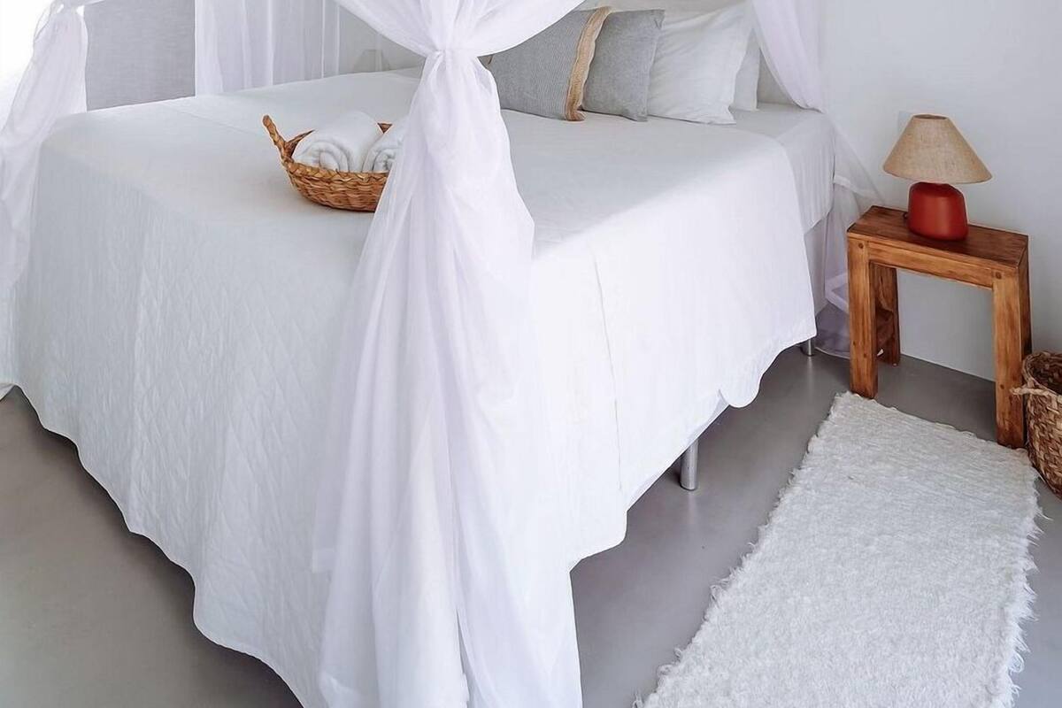 A bedroom with a canopy bed, a bedside table with a lamp, and a small rug.