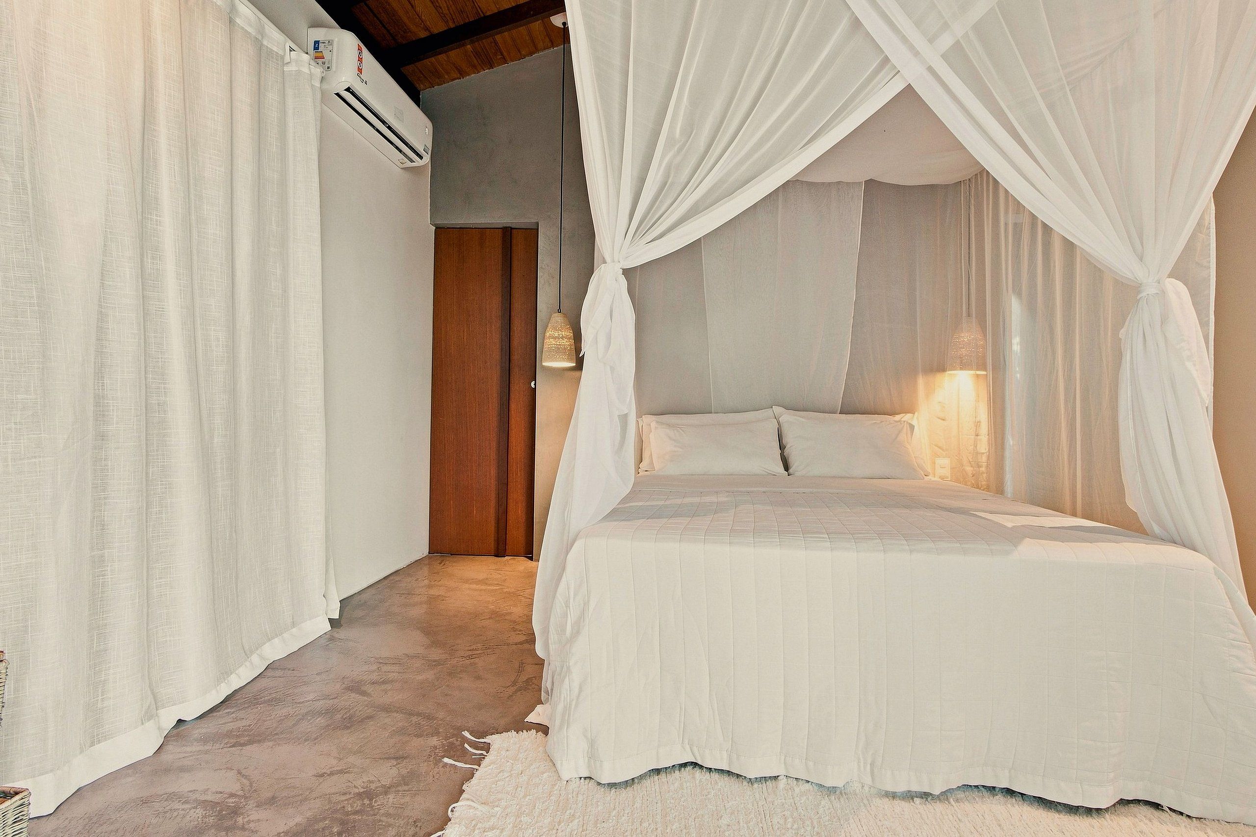 A bedroom with a canopy bed, white curtains, and a visible air conditioning unit.