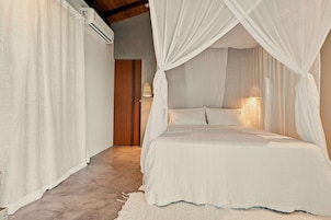 Una camera da letto con un letto a baldacchino, tende bianche e un condizionatore d'aria a vista.