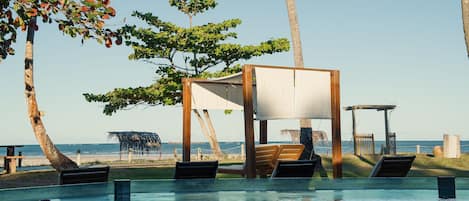 An outdoor pool area with lounge chairs and a wooden structure providing shade.
