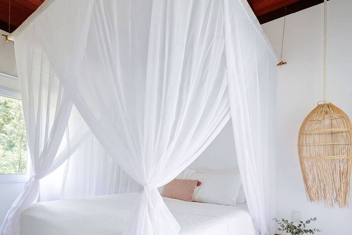 A room with a bed under a white canopy, a wooden bench, and a woven hanging chair.