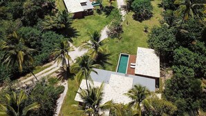 Vista aérea de un resort con varias construcciones tipo cabaña, una piscina y una playa al fondo.