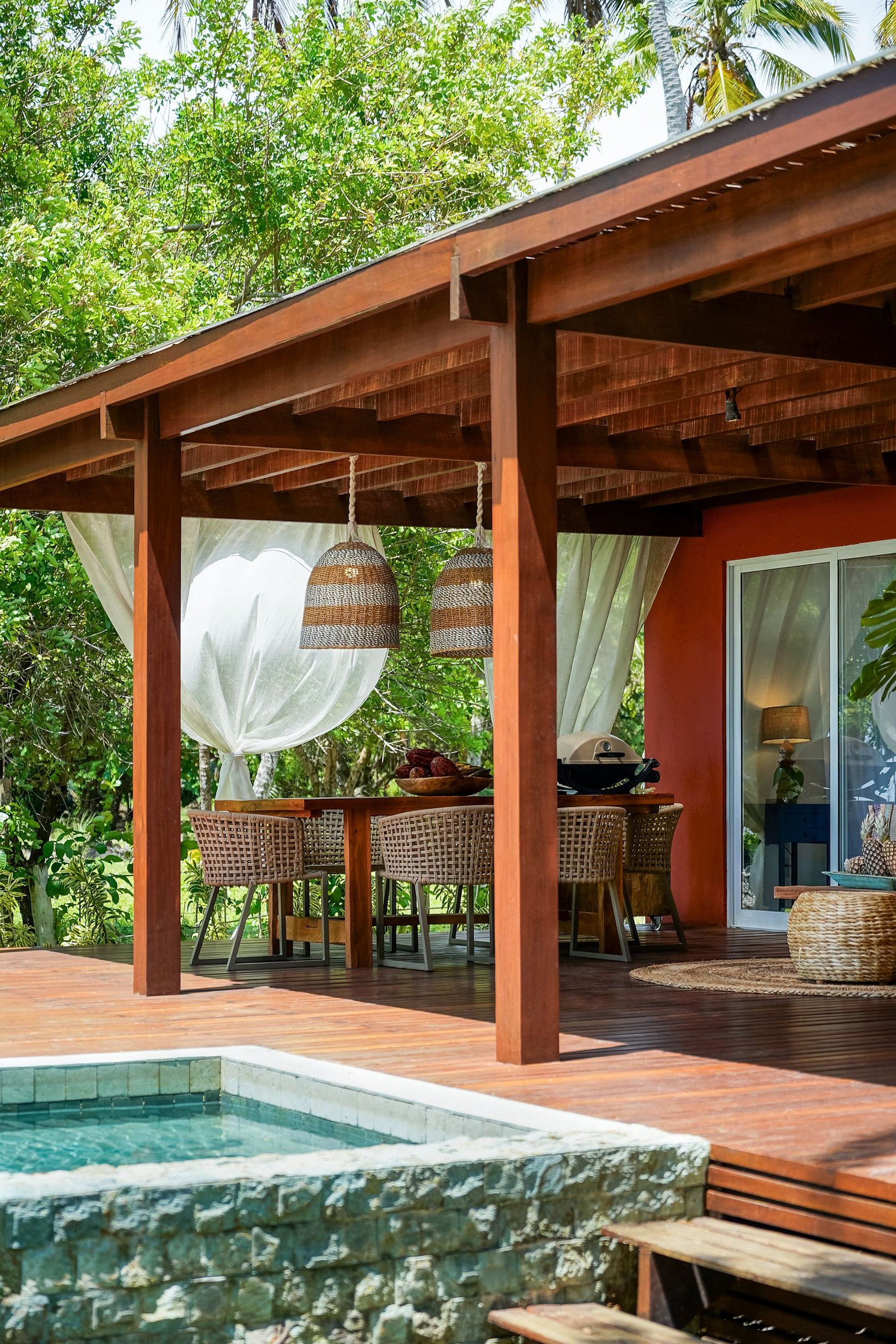 A covered outdoor area with a pool, wicker furniture, and a dining table.