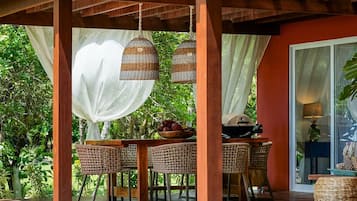 A covered outdoor area with a pool, wicker furniture, and a dining table.