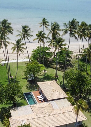 Um imóvel à beira-mar com piscina, palmeiras e vista para o oceano.