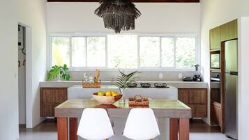Une cuisine moderne dotée d’une grande fenêtre, de meubles en bois, d’un îlot central avec des chaises et d’un luminaire suspendu.