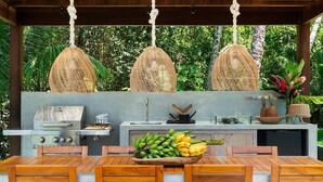 Una cocina exterior con una parrilla, un cuenco de fruta y cestas de mimbre colgantes.