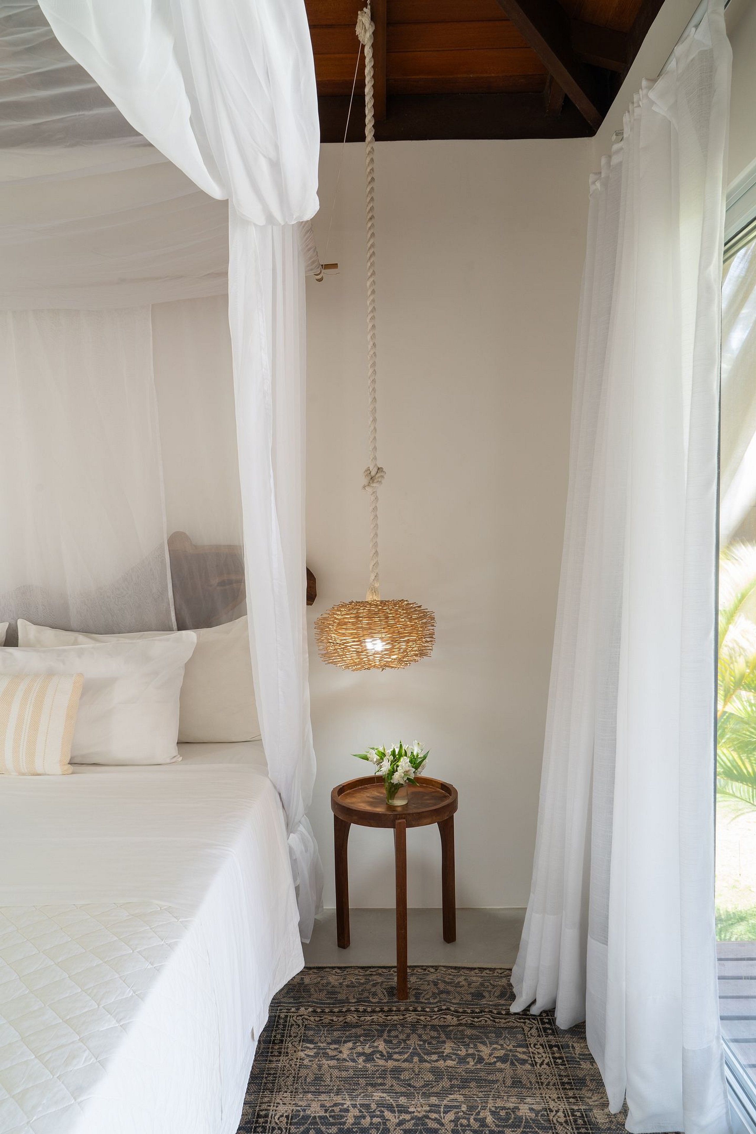 A bedroom with a canopy bed, a hanging light fixture, and a small table with a plant.
