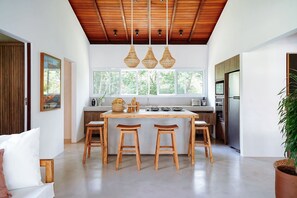 A modern kitchen with a wooden ceiling, a central island with stools, and large windows. - Orixás Residence (Cairu)