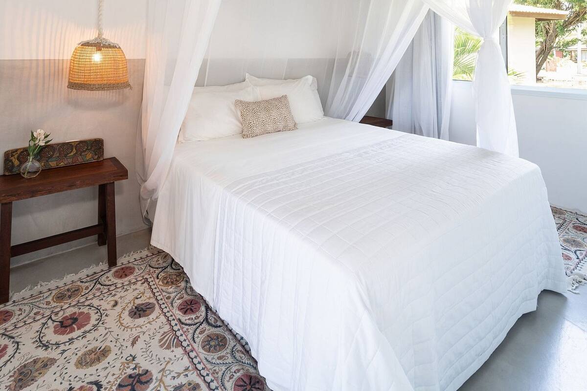 A bedroom with a canopy bed, a bedside table with a lamp, and a patterned rug.