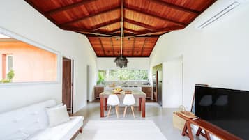 Een moderne woonkamer met een houten plafond, een witte bank, een eettafel met stoelen en een grote flatscreen televisie.