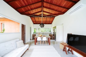 Un salon moderne avec un plafond en bois, un canapé blanc, une table à manger avec des chaises et un grand téléviseur à écran plat.
