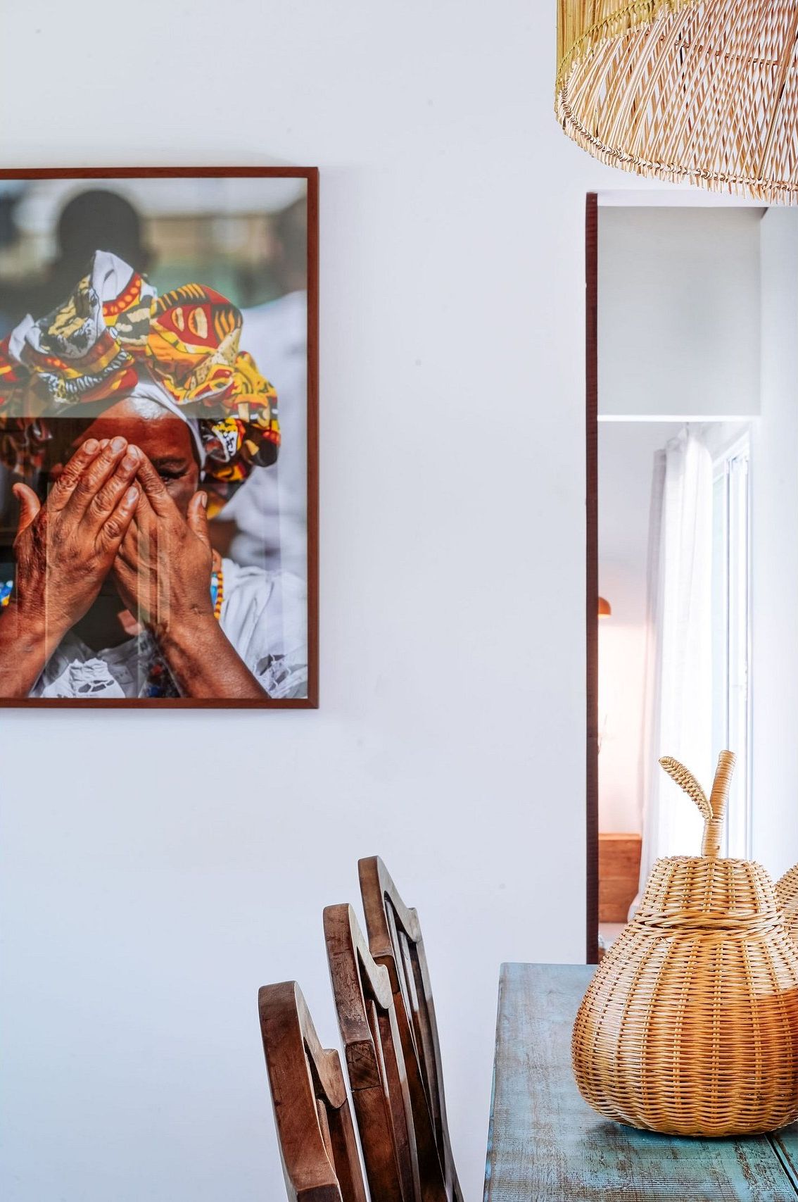 Una fotografía enmarco en la pared, una cesta de mimbre sobre una mesa y una silla de madera.