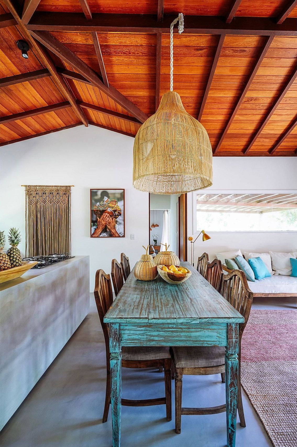 A dining area with a rustic wooden table, woven pendant light, and a view of the outdoors.