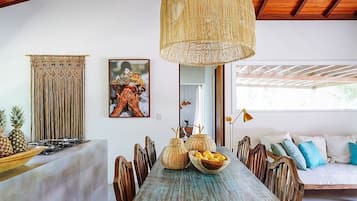 A dining area with a rustic wooden table, woven pendant light, and a view of the outdoors.