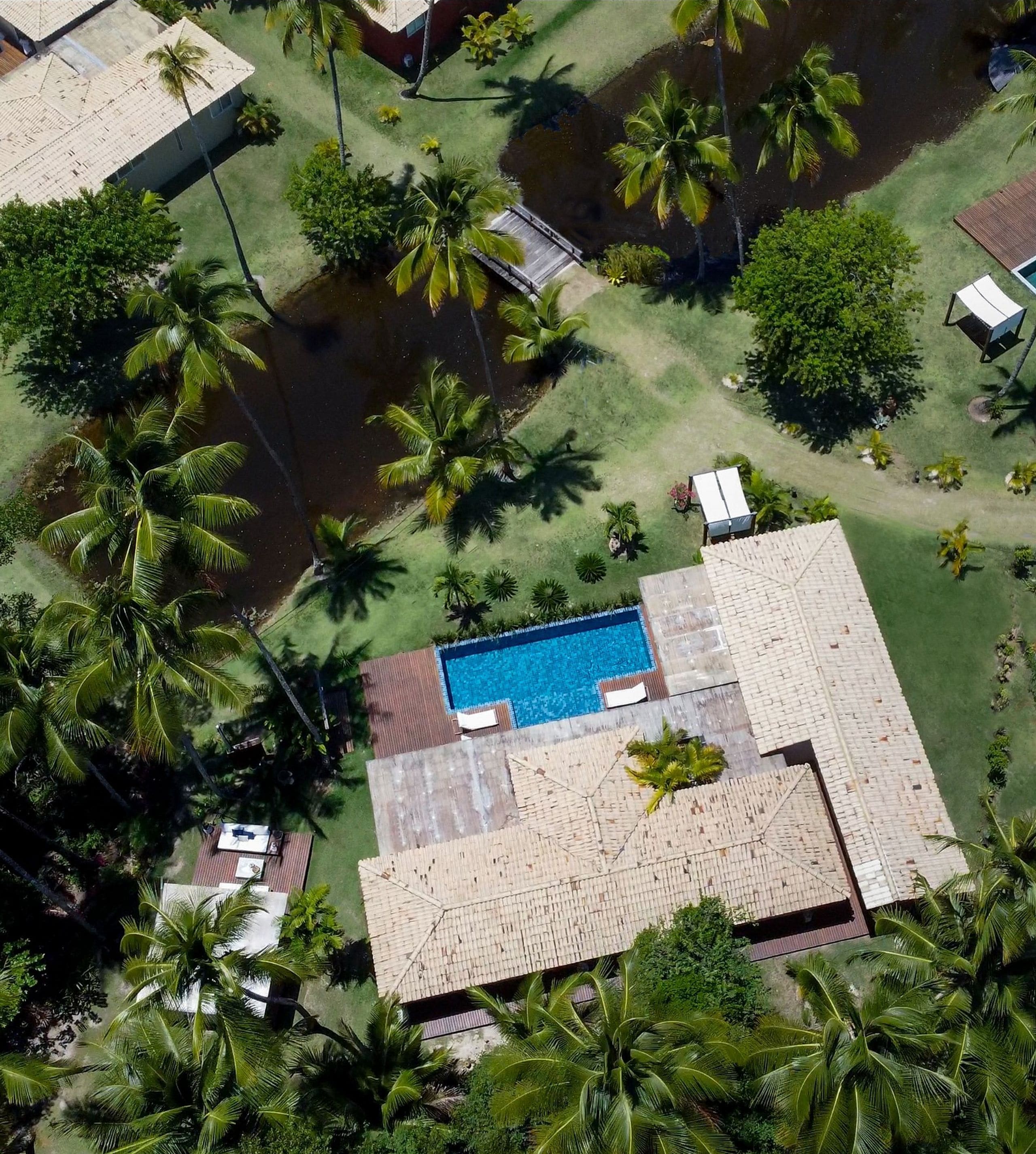 Vista aérea de um resort com piscina, palmeiras e céu azul límpido.